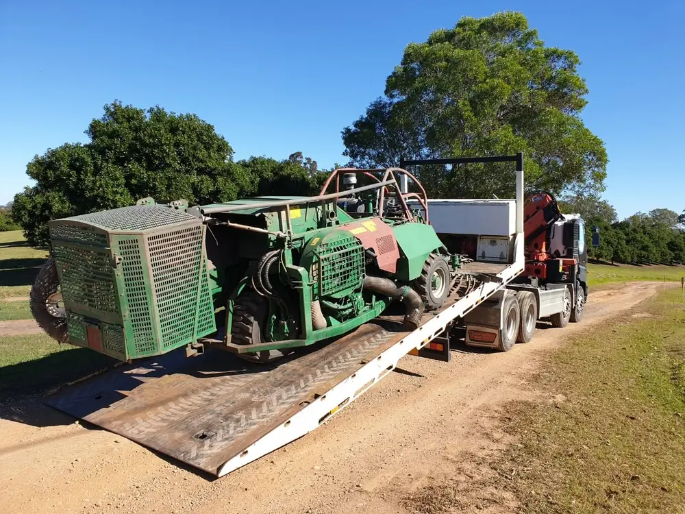 Large green machinery loaded onto the tilt tray of a crane truck